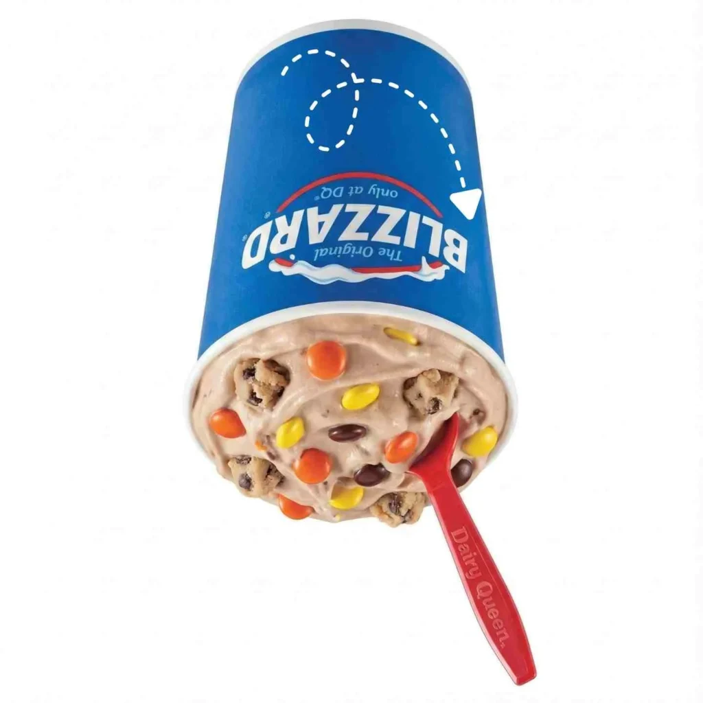REESE'S PIECES Cookie Dough Blizzard Treat held upside down showing vanilla soft serve mixed with REESE'S PIECES candies and chocolate chip cookie dough pieces
